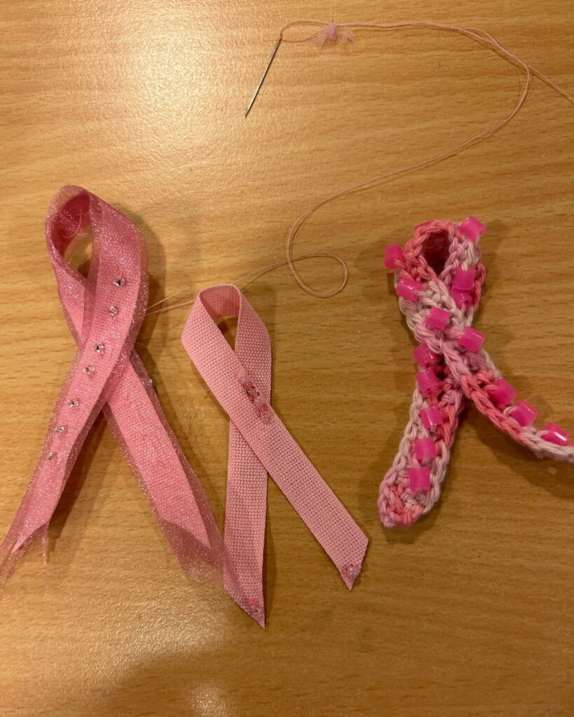 Tre rosa band i olika utföranden, rosa tråd med nål och ett flätat band dekorerat med rosa pärlor
