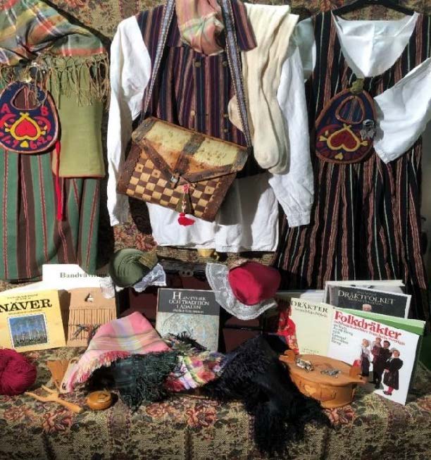Utställning med svenska folkdräkter, väskor, textilier, mössor och böcker om hemslöjd