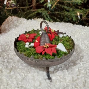 Juldekoration i metallfat med mossa, röda julblommor, vita bär och små figurer
