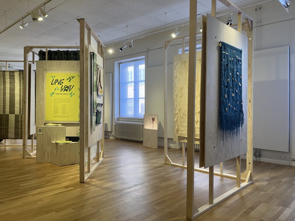 Utställning med vävda textilier i träställningar, bland annat färgstarka blå, gula och gröna vävar