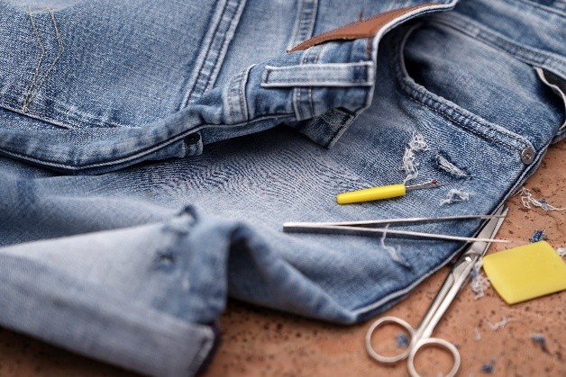 Jeans som lagas med synålar, tråd och sax på ett arbetsbord