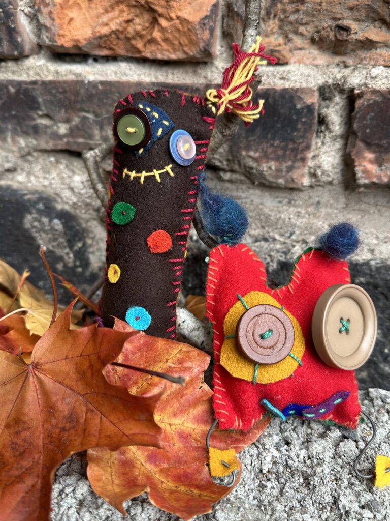 Handsydda halloweenfigurer av filt, dekorerade med knappar och färgglada stygn bland höstlöv