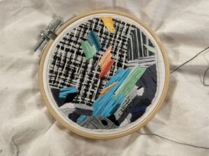 Broderi i en rund träbåge med färgglada trådar på svartvit väv