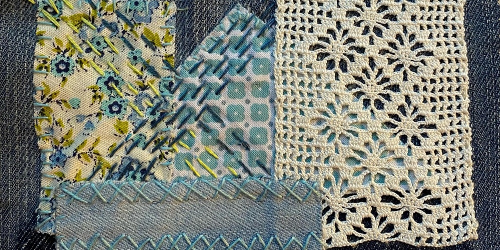 Närbild av textilt återbruk med broderade tygbitar, dekorativa sömmar och virkad spets