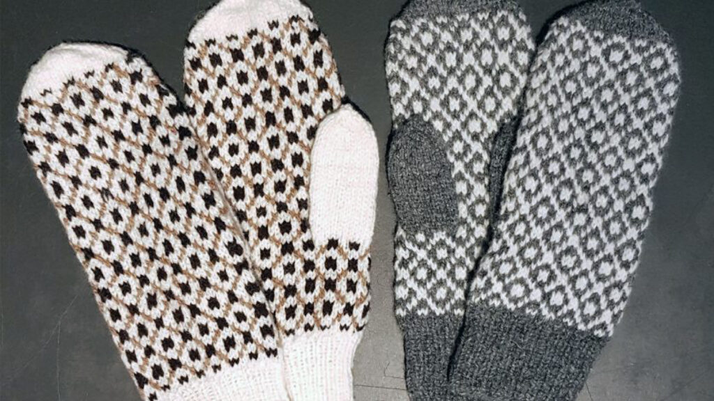 Två par handstickade vantar med svartvita mönster; ett par i vitt och brunt, det andra i grått