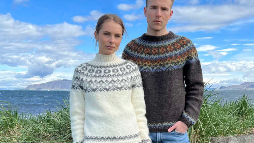 Två personer bär handstickade tröjor med traditionella nordiska mönster vid havet