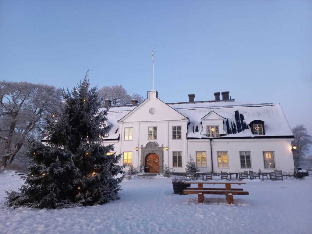 Snötäckt herrgård med julpyntad gran och svensk flagga