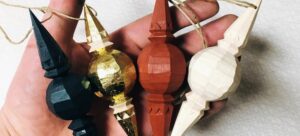 Hand håller fyra handtäljda juldekorationer i svart, guld, rött och vitt trä