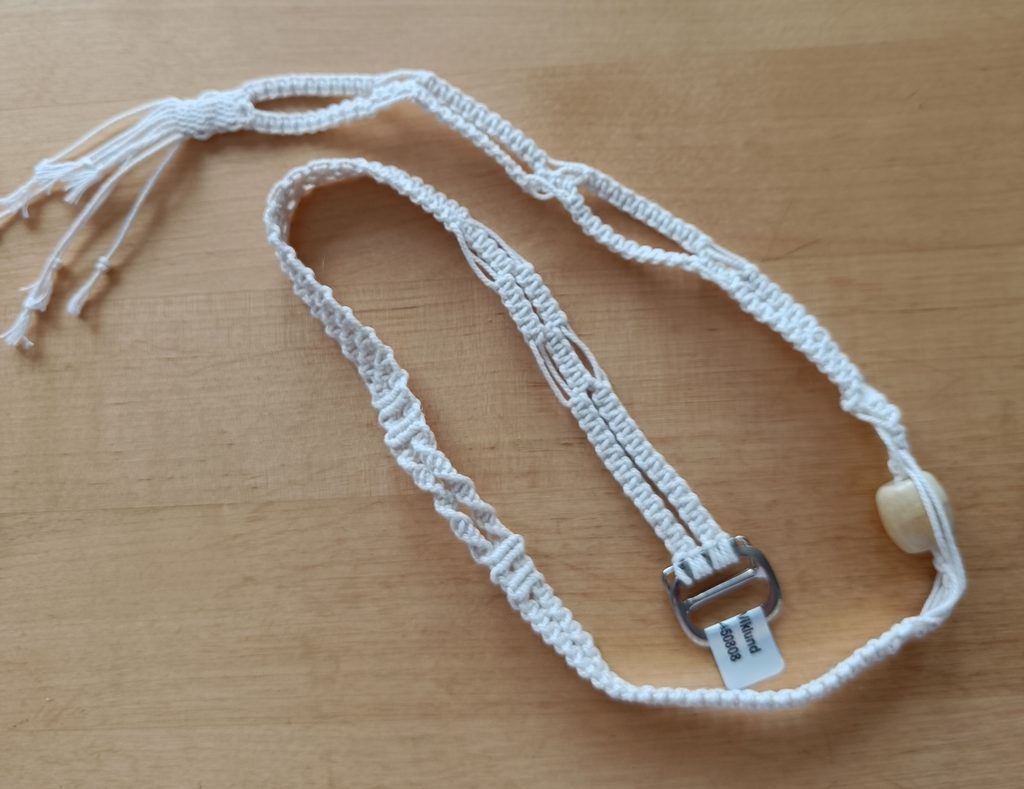 Vitt handvirkat band med spänne och träpärla på ett träbord