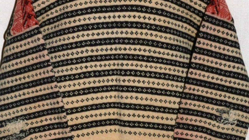 Närbild av ett mönstrat textilhantverk med svarta och beige ränder, små blommotiv och röda detaljer