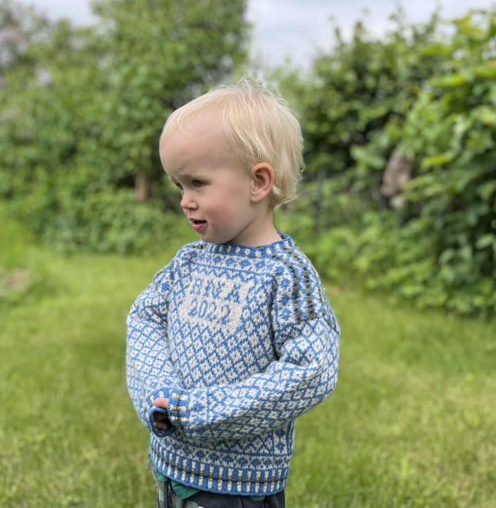Barn i en blåvit mönsterstickad tröja utomhus