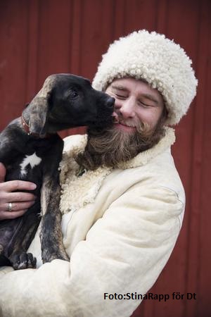 Hund pussar en glad och skäggig man i vit pälsmössa