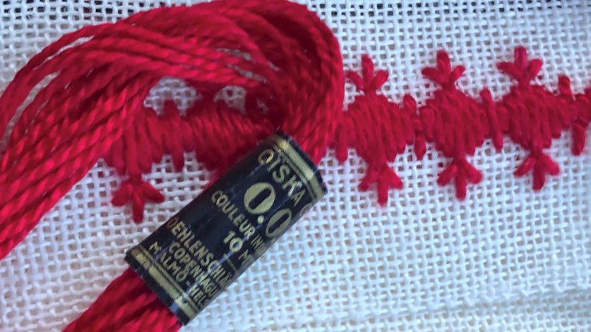 Rött garn och rött broderi mot vit bakgrund