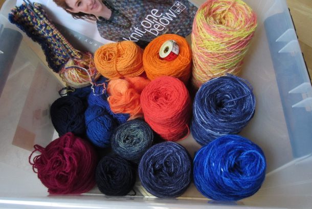Plastback med garner i olika färger samt boken "knit one below".
