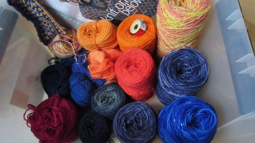 Plastback med garner i olika färger samt boken "knit one below".