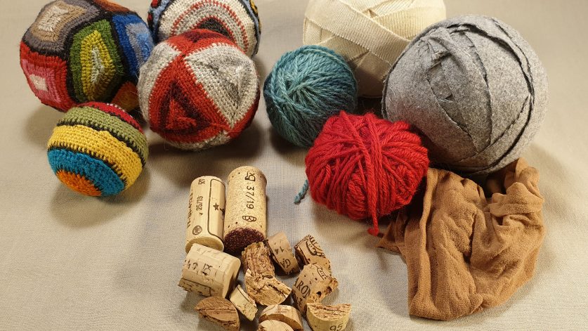 Handgjorda bollar som är gjorda av textilmaterial och broderade med ullgarn. Bredvid ligger vinkorkar, garnnystan och rullar med tygremsor.