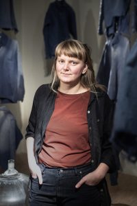 Helena Bratt stående i ett verk med titeln "Lukta hemma" som är en installation av gamla slitna arbetskläder från en mjölkgård i Hälsingland.