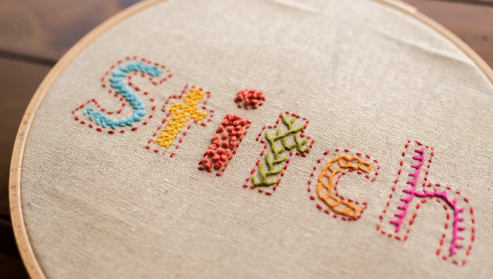 Bokstäverna STITCH broderade på vitt tyg